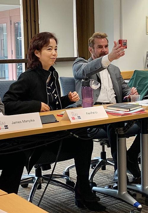 Fei-Fei Li, científica de inteligencia artificial, sentada a una mesa redonda de Stanford HAI junto a un cartel con su nombre, entre otros tres panelistas