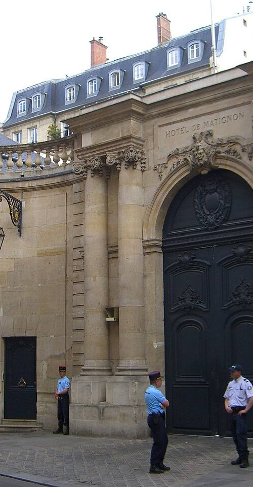 Verja de entrada del Hôtel de Matignon en París, con "HOTEL DE MATIGNON" tallado en piedra sobre la puerta y dos gendarmes franceses de guardia en el acceso