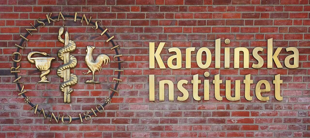 Placa dorada con el emblema y el nombre "Karolinska Institutet, Anno 1810" sobre un muro de ladrillo rojo, en la entrada principal del campus de Solna