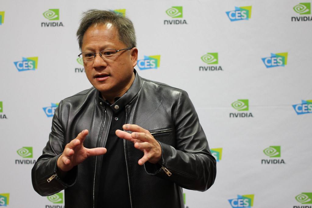 Retrato de Jensen Huang, CEO de Nvidia, hablando en un escenario con un fondo tecnológico.