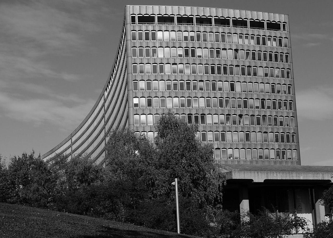 Fachada curva de hormigón de la torre que alberga la sede de la Organización Internacional del Trabajo en Ginebra, fotografiada en contrapicado desde uno de sus laterales con arbolado en primer término