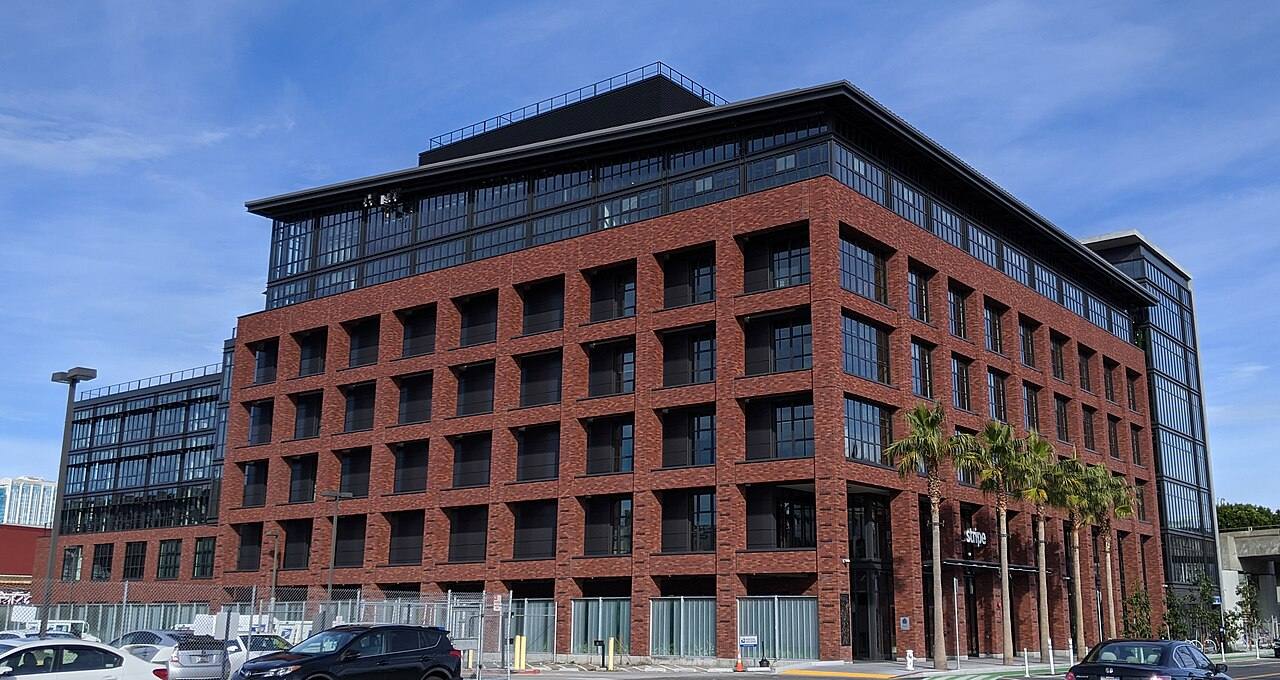 Edificio de ladrillo de la sede de Stripe en San Francisco, con el rótulo "stripe" sobre la entrada y palmeras junto a la puerta principal