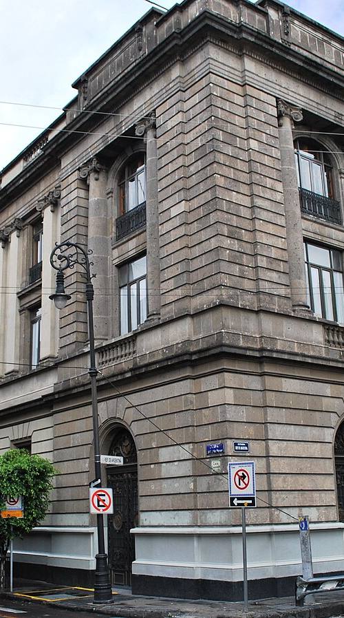 Esquina del edificio histórico de la Secretaría de Educación Pública (SEP) en el Centro Histórico de la Ciudad de México, con la torre de un antiguo convento al fondo y peatones en la acera.