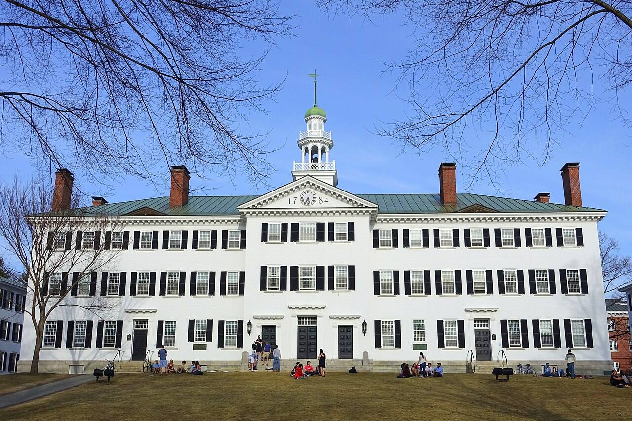 Dartmouth Hall, el edificio histórico de columnas blancas y cúpula de Dartmouth College en Hanover, New Hampshire, con la fecha 1784 tallada sobre la entrada y estudiantes sentados en el césped frente a la fachada