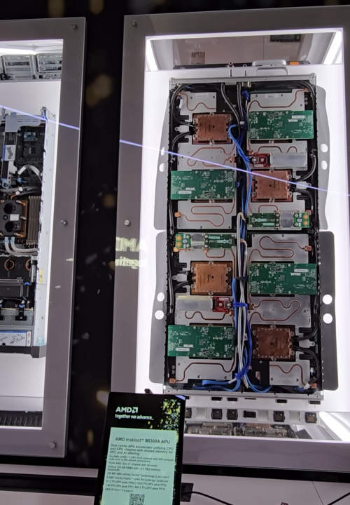 Cartel oficial de AMD con las especificaciones del acelerador Instinct MI325X, junto a la vitrina que exhibe el hardware real refrigerado por líquido en el stand de AMD durante el CES 2025