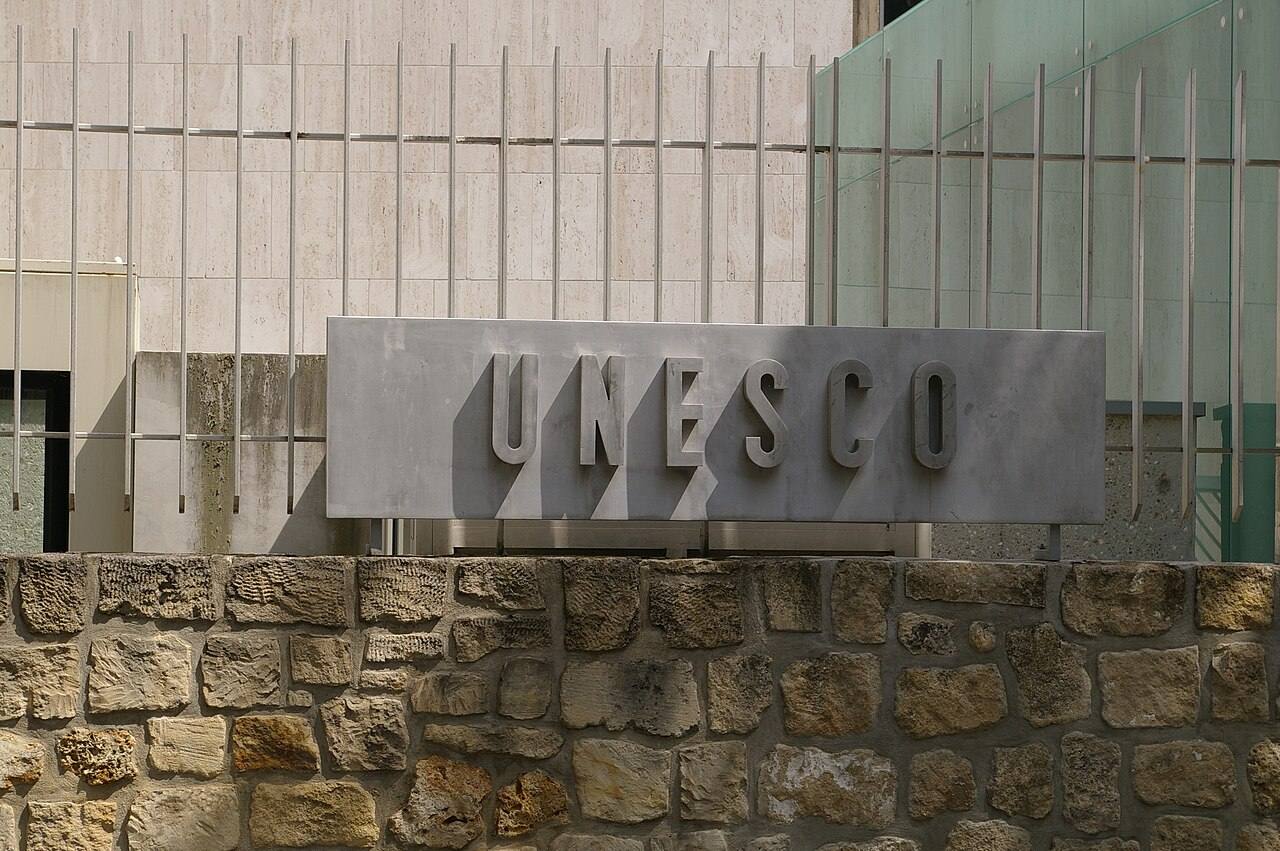 Placa metálica con el nombre UNESCO sobre la fachada de piedra de su sede en París, tras la verja perimetral del edificio
